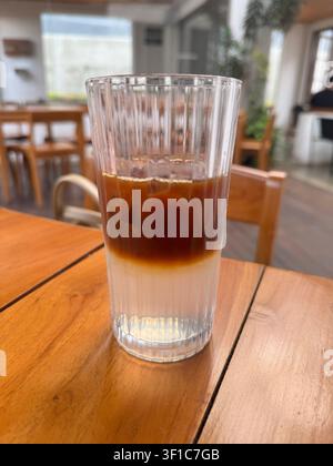 Schichtweiser gekühlter Zitronengras-Americano, serviert in einem klaren Glas vor dem Umrühren, mit Espresso und frischer Zitronengras-Infusion auf einem Holztisch in einem Mod Stockfoto