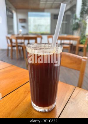Erfrischender Eiskaffee Americano in einem klaren Glas mit Eiswürfeln auf einem Holztisch in einem modernen Café serviert, der einen gekühlten Spezialkaffee bietet Stockfoto