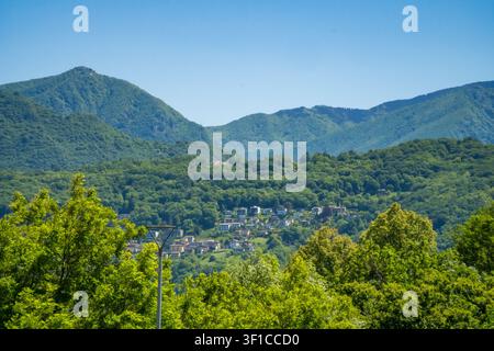 Ein kleines Dorf, eingebettet zwischen üppigen grünen Bergrücken, eingerahmt von Waldkronen, in der Region Malcantone im Tessin, Schweiz. Stockfoto