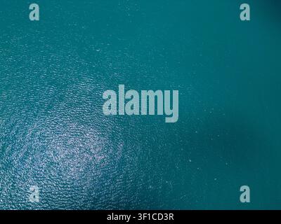Droneshot, der direkt auf das schimmernde türkisfarbene Meerwasser blickt. Schöne Sonnenreflexe und kleine Wellen auf der ruhigen tiefen Meeresoberfläche. Stockfoto