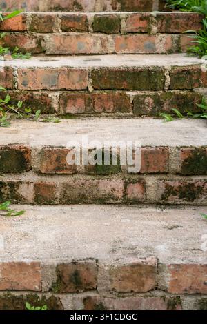 Eine Nahaufnahme von gealterten Ziegelstufen mit abgenutzten Betonbelägen, die rustikale Texturen und verwitterte Oberflächen zeigen Stockfoto