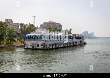 Kairo, Ägypten, 25.07.21. Fischerboot - Abouzeid schwimmendes Restaurantboot, das am Ufer des Nils angelegt hat, mit der Kairoer Stadtlandschaft im Hintergrund. Stockfoto