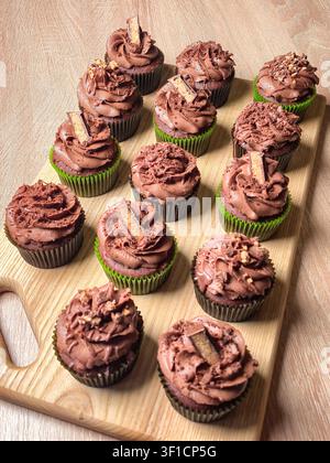 Eine entzückende Auswahl an frisch gebackenen Schokoladencupcakes, die mit cremiger Glasur überzogen und mit Schokoladenstücken und Nüssen garniert sind, präsentiert auf einem r Stockfoto