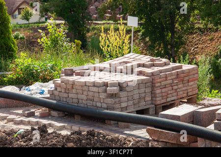 Ein großer Stapel rechteckiger Pflastersteine liegt auf Holzpaletten und wartet auf die Verlegung für einen Gartenweg oder eine Terrassenkonstruktion Stockfoto