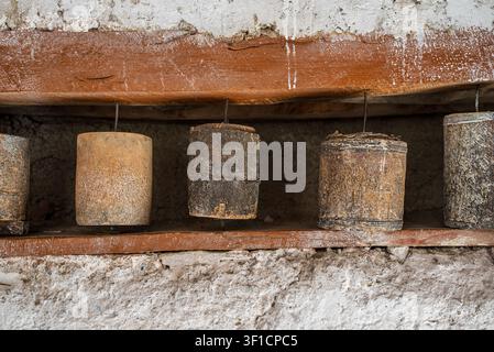 Detail einer Reihe alter tibetischer Gebeträder aus abgenutztem Holz, die in einer Nische zwischen braunen Balken und einer rauen Steinwand platziert sind. Die rituellen Zylinder sho Stockfoto