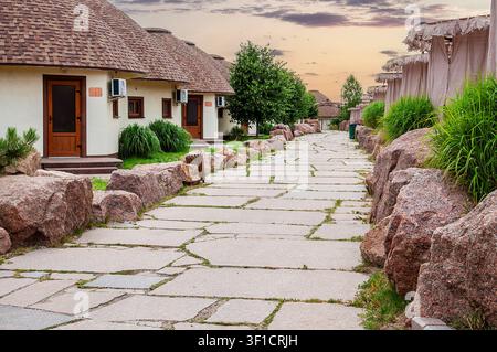 Ein malerischer Steinweg windet sich durch ein Resort mit charakteristischen Bungalows mit kegelförmigen Dächern und lebendiger natürlicher Landschaftsgestaltung Stockfoto