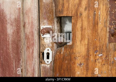 Alte verwitterte Holztür mit rostigem antiken Metallgriff und Schlüsselloch Stockfoto
