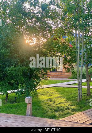 Holzhütten, umgeben von üppigen Bäumen und grünem Rasen im warmen Abendsonnenlicht. Stockfoto