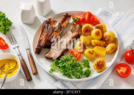 Amerikanische gegrillte Schweinerippchen aus dem Hinterhof mit ganzen Kartoffeln, frischen Gartentomaten, lockiger Petersilie und klassischem amerikanischem gelbem Stadion-Senf auf Weiß Stockfoto