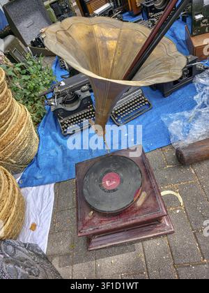 XALO, SPANIEN - 20. JUNI 2026. Menschen versammeln sich auf einem antiken Flohmarkt im Freien, um das authentische Retro-Grammophon zu betrachten. Das Messinghorn glänzt im Sonnenlicht, während Stockfoto