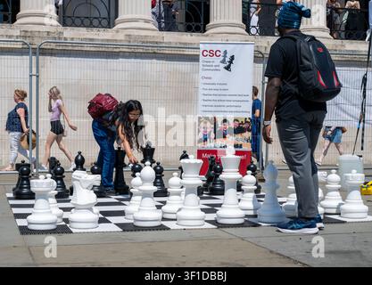 Ein junges Paar spielt riesiges Schach im Freien beim ChessFest am Trafalgar Square London 2026 neben einem CSC Chess in Schools and Communities Werbebanner Stockfoto