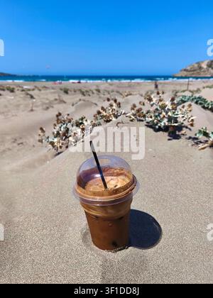 Frappe Kaltes Erfrischungsgetränk Eiskaffee an einem sandigen Strand. Freddo Espresso Erfrischung im Sommer. Strandschirme in einem Ferienort. Frape. Stockfoto