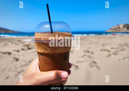 Frappe Kaltes Erfrischungsgetränk Eiskaffee an einem sandigen Strand. Freddo Espresso Erfrischung im Sommer. Strandschirme in einem Ferienort. Frape. Stockfoto