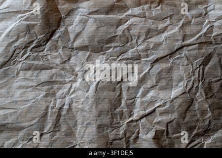 Zerknitterter brauner Kraftpapierhintergrund, Nahaufnahme. Zerknitterte und zerknüllte braune Bastelpapiertextur mit tiefen Falten, Schatten und Highlights repr Stockfoto