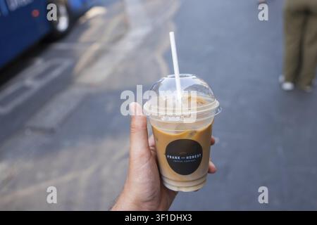 Hand, die einen Eiskaffee in einem Plastikbecher mit Strohhalm auf einer Straße in der Stadt Greystones, Irland, hält Stockfoto