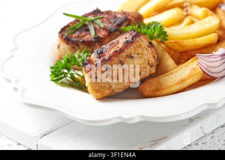 Gebratene Schweinerippchen mit Pommes frites und frischen Tomaten. Heller Hintergrund. Kopierbereich. Stockfoto