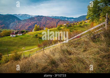 Bewundernswerte herbstliche Landschaft mit schneebedeckten Bergen im Hintergrund. Niedliche kleine Häuser am Hang, Karpaten, Siebenbürgen, Rumänien, Europa Stockfoto