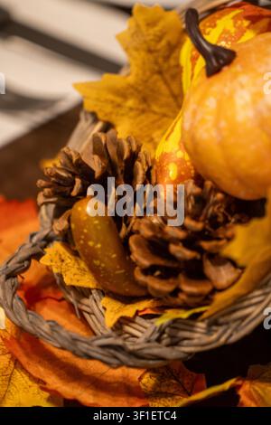 Ein warmes Nahaufnahme-Foto eines geflochtenen Weidenkorbs gefüllt mit kleinen dekorativen Kürbissen, Flaschenkürbissen, Tannenzapfen und lebhaften Herbstblättern Stockfoto