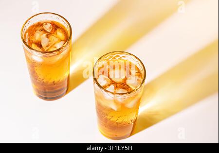 Gläser mit eisgekühltem Apfelsaft mit goldenen Schatten auf hellem weißem Sommergetränkehintergrund Stockfoto