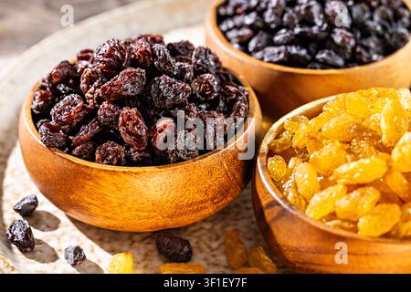 Nahaufnahme von Rosinen-Sortiment mit goldenen schwarzen und dunklen Rosinen in Holzschüsseln als gesunder Trockenobst-Snack Stockfoto