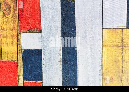 Kühne geometrische Blöcke in Rot, Gelb, Marineblau und Weiß bilden eine auffällige abstrakte Komposition mit verwitterten Texturen. Die bemalte Holzoberfläche zeigt Alter Stockfoto