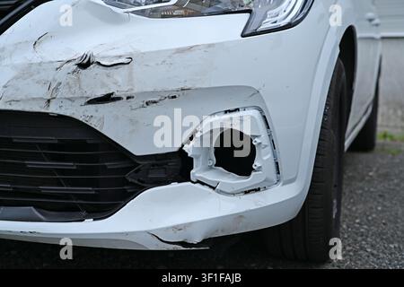 Beschädigte Frontstoßstange eines weißen Autos nach einem Verkehrsunfall, Nahaufnahme mit Kratzern. Stockfoto