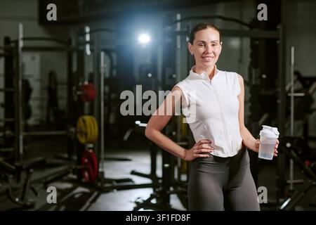Porträt einer jungen, fitten Frau, die im Fitnessstudio einen Protein-Shake hält Stockfoto