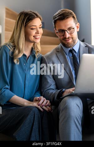 Zwei glückliche, vielseitige Mitarbeiter aus verschiedenen ethnischen Geschäftsbereichen, die im Büro des Unternehmens arbeiten und sich unterhalten Stockfoto