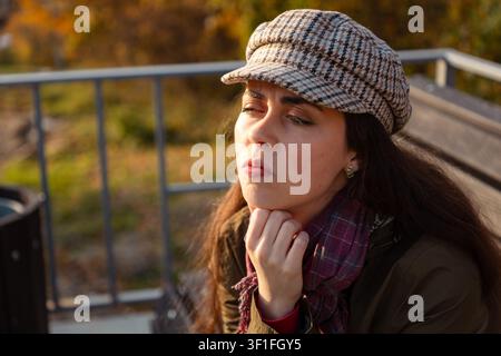 Eine schöne Frau sitzt im Freien, stützt ihr Kinn auf die Hand und blickt nachdenklich im Licht der goldenen Stunde weg Stockfoto