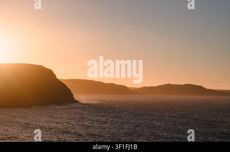 Silhouetten küstennaher Hügel von Neufundland während eines goldenen Sonnenuntergangs Stockfoto