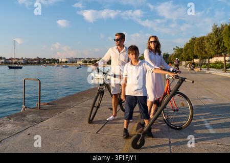 Familie radelt an der Uferpromenade in Umag Eltern und Sohn mit Fahrrädern und E-Scooter Stockfoto
