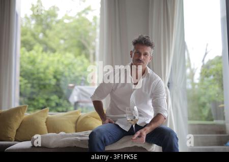Stylischer Mann entspannt sich zu Hause mit einem Glas Wein Stockfoto