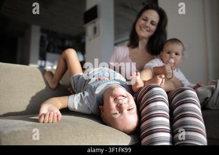 Lächelnde Mutter entspannt sich auf der Couch mit zwei Kindern Stockfoto