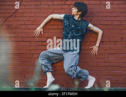 Junger Mann in einer dynamischen Tanzpose vor einer Ziegelmauer Stockfoto