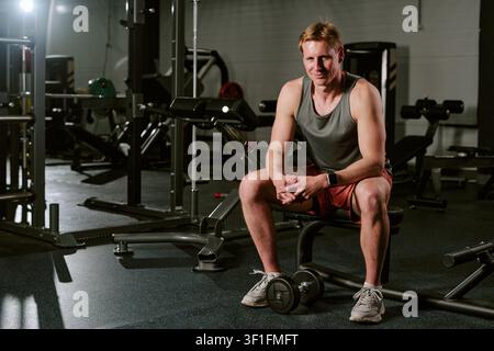 Porträt eines jungen erwachsenen männlichen Athleten, der nach einem Krafttraining auf einer Bank sitzt Stockfoto