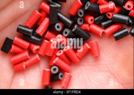 Kleine rote und schwarze zylindrische Plastikkügelchen mit hohlen Mittelstücken, die in einer Hand gehalten werden. Stockfoto
