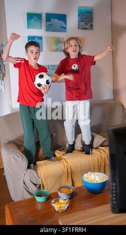 Jungen springen auf der Couch und jubeln begeistert, während sie ein Fußballspiel anschauen Stockfoto