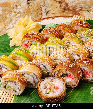 Ein großes Tablett zeigt eine Auswahl an Sushi-Rollen in verschiedenen Farben, darunter mehrere Arten von Füllungen, und garniert mit Ingwer auf einer Bambusmatte. Stockfoto