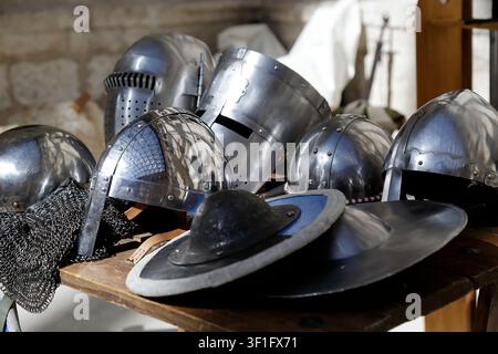 Sammlung mittelalterlicher Metallhelme, die auf einem Holztisch in einer historischen Umgebung ausgestellt sind. Stockfoto