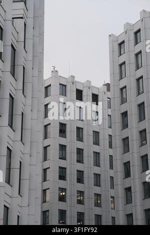 Moderne weiße Mehrgeschossbauten mit großen Fenstern unter bewölktem Himmel. Urbane Architektur aus niedriger Blickwinkelansicht. Stockfoto