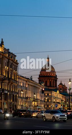 Abendansicht der Kathedrale St. Isaak und historischer Gebäude entlang einer belebten Straße. Autos, Straßenbahndrähte und goldene Kuppel zur Blauen Stunde Stockfoto
