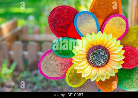 Bunter Sonnenblumen-Windspiel mit Regenbogen-Glitzerblättern auf einem unscharfen Gartenzaun-Hintergrund im Nahaufnahme Stockfoto