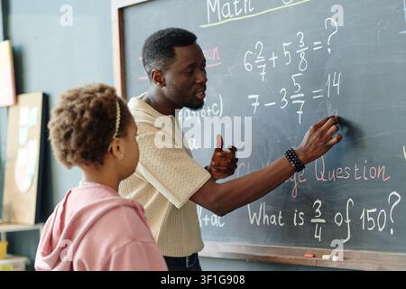 Schwarzer männlicher Lehrer erklärt einer Schülerin eine Mathematikstunde im Klassenzimmer Stockfoto