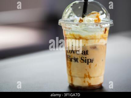 Schräger Blick auf ein gekühltes Karamell-Kaffee-Getränk mit Sahne und Sirup in einem Plastikbecher mit Deckel Stockfoto