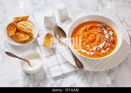 Deutsche Süßkartoffelsuppe garniert mit Sahne und Samen in einer weißen Schüssel, serviert mit einem Löffel auf einer Serviette und geröstetem Brot, nicht KI-generiert Stockfoto