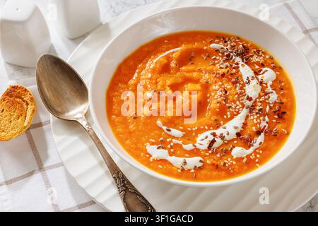 Deutsche Süßkartoffelsuppe, gesüßte Kartoffelsuppe, garniert mit Sahne und Samen in einer Schüssel, serviert mit einem Löffel auf einer Serviette und geröstetem Brot, nicht KI-generiert Stockfoto