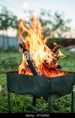 Hell brennendes Feuer mit Holzscheiten in einem Metallbrazier im Freien Stockfoto