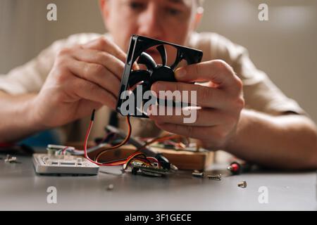 Mann hält einen Kühlventilator, verbindet Drähte und montiert elektronische Teile für die Reparatur und Wartung von Computerhardware in der Werkstatt. Konzept von Stockfoto