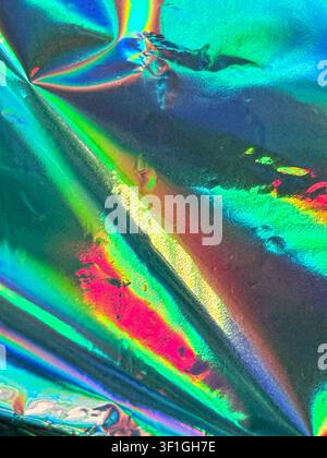 Abstrakter strukturierter Hintergrund mit zerknittertem, irisierendem Folieneffekt. Reflektierende Oberfläche zeigt ein lebendiges Farbspektrum inklusive Grün, Blau, Rosa, a Stockfoto