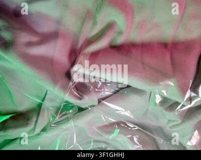 Nahaufnahme einer Stofftextur mit lebhaftem rosa und grünem Batikmuster. Weiche Stofffalten erzeugen Tiefe, wobei klarer Plastikfolie Glanz und Reflexion hinzufügt Stockfoto